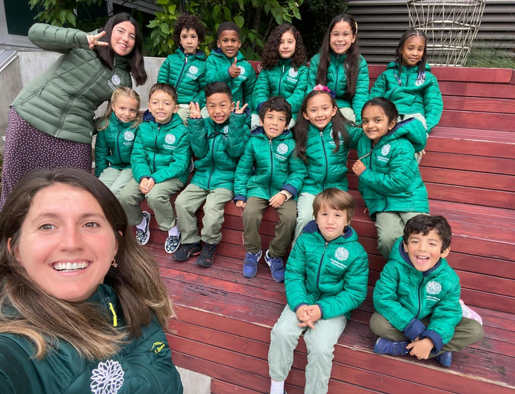 Group of children and adults in matching green jackets sitting on wooden steps