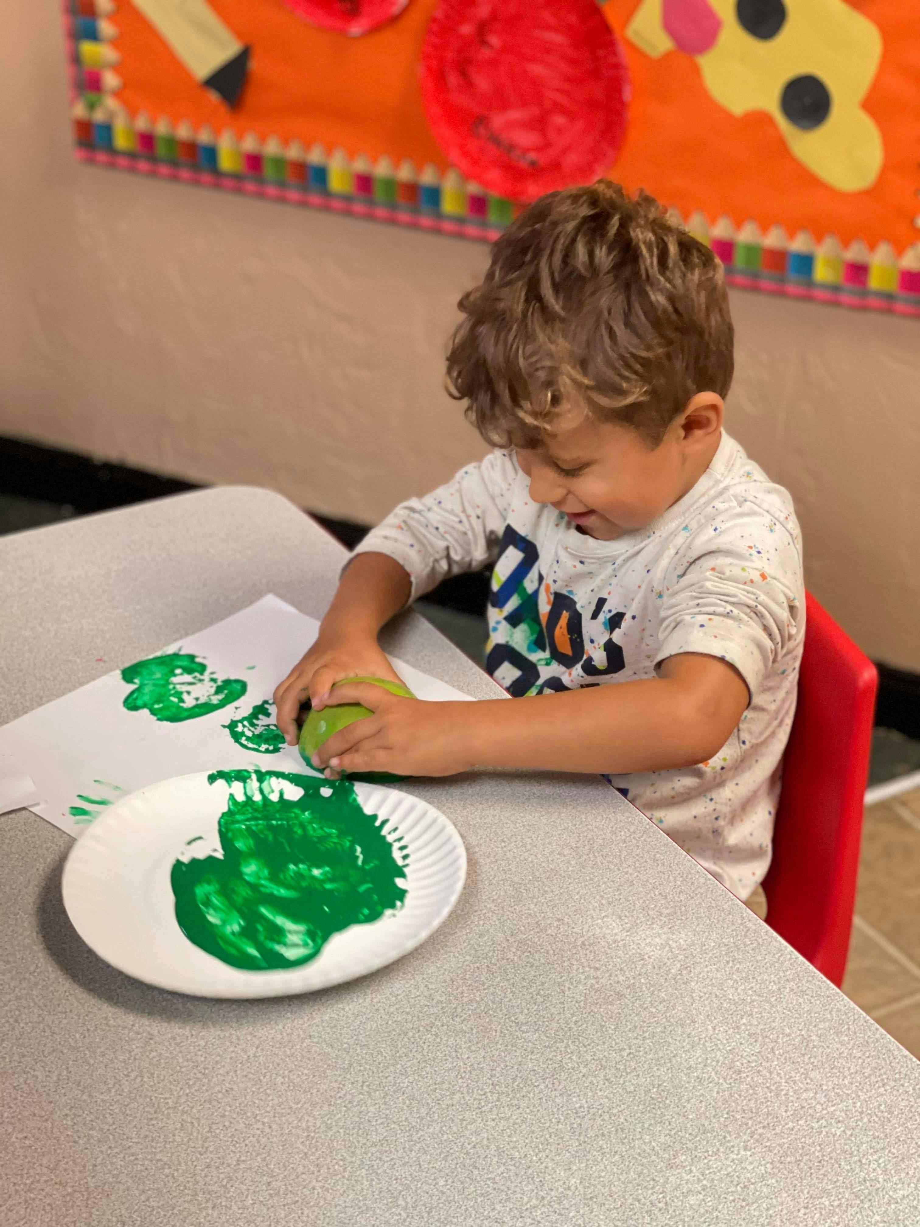 Child doing apple printing with green paint