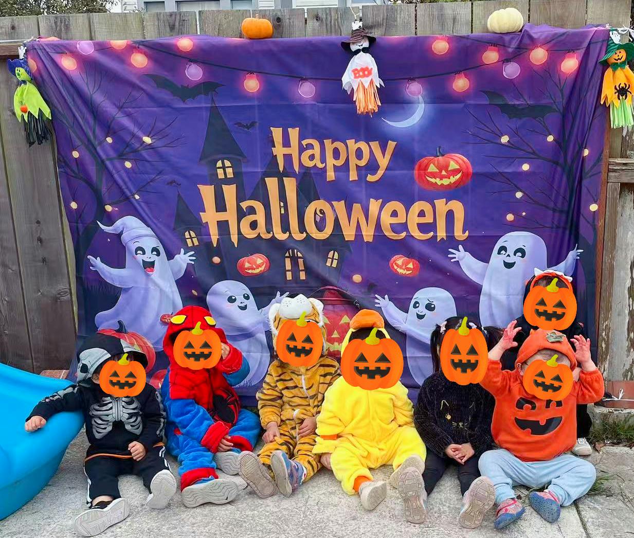 Children in pumpkin costumes sitting in front of a Happy Halloween banner