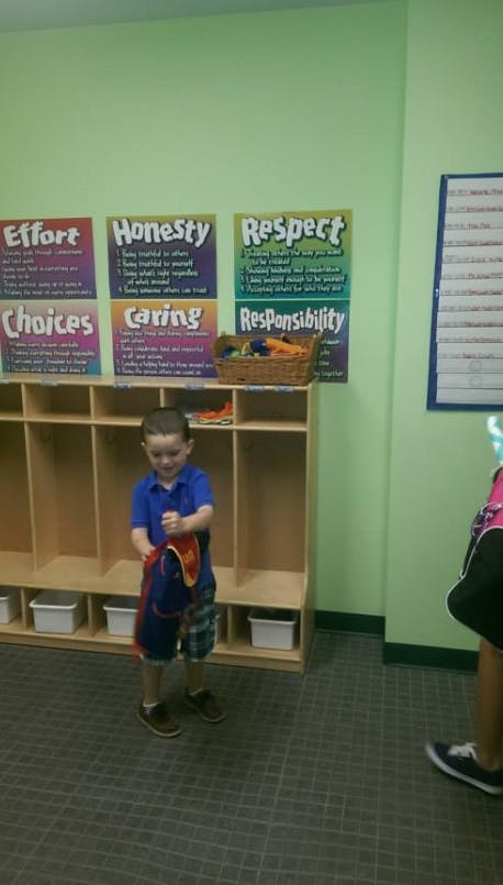 Child standing in front of cubbies, holding a red and blue item
