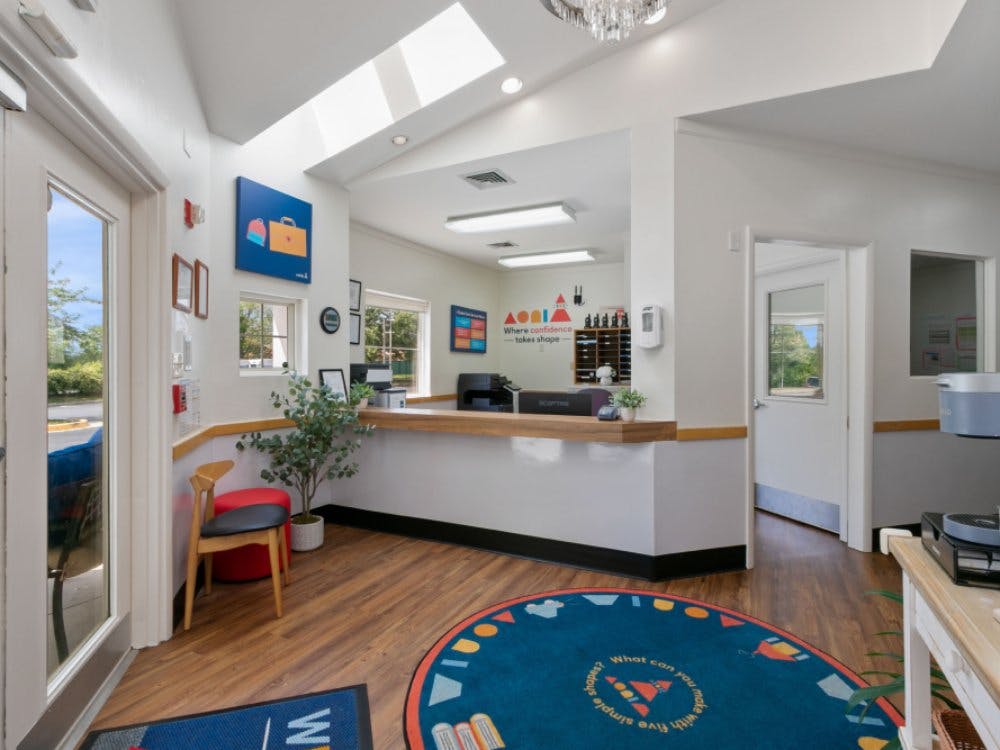 An empty reception area with a desk, chairs, and a round blue rug on a wooden floor