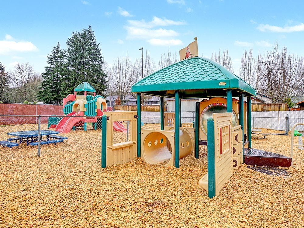 A playground with two plastic playsets and wood chips on the ground