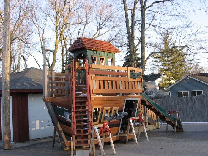 Wooden playground structure shaped like a ship with a slide and ladder