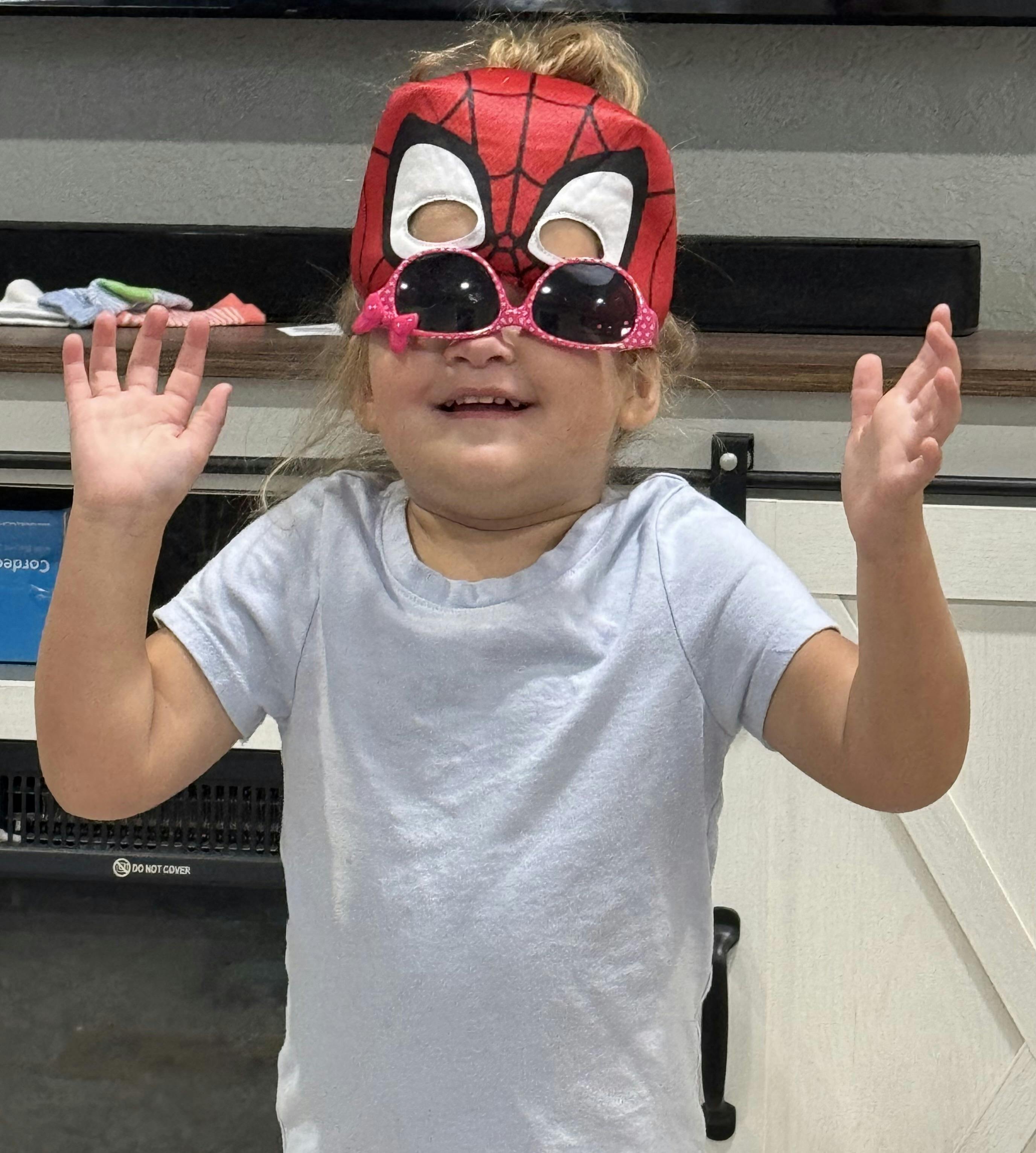 Child wearing a Spider-Man mask and sunglasses with hands raised