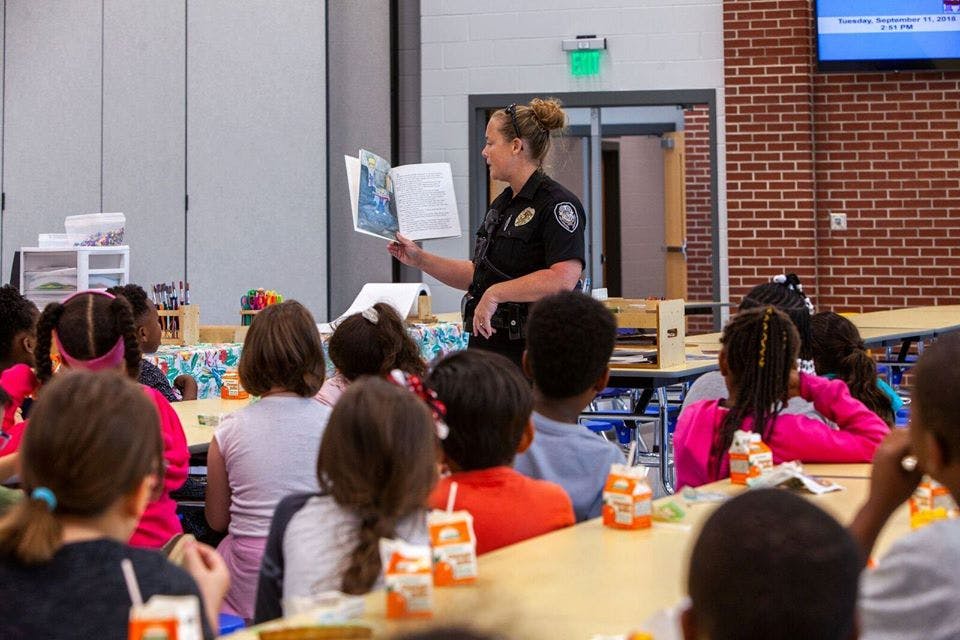 Person in uniform reading a book to children in a classroom