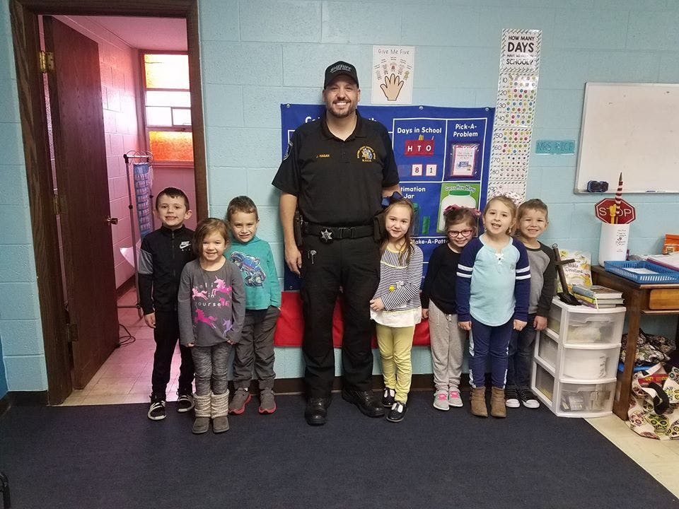 Adult in uniform standing with a group of children in a classroom