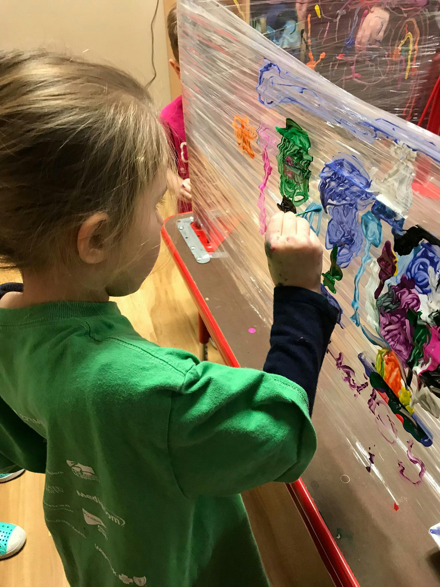 Child painting on a clear surface with colorful paints
