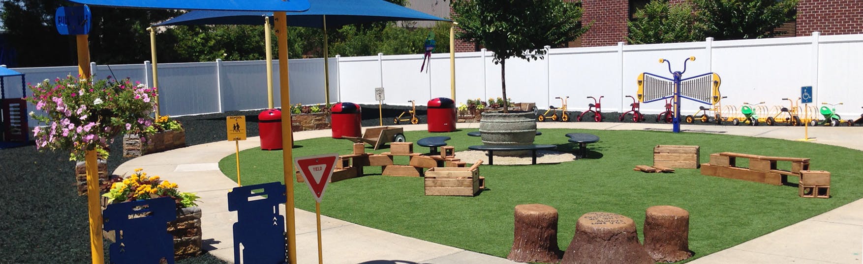 Outdoor play area with artificial grass, shade structure, and various play elements