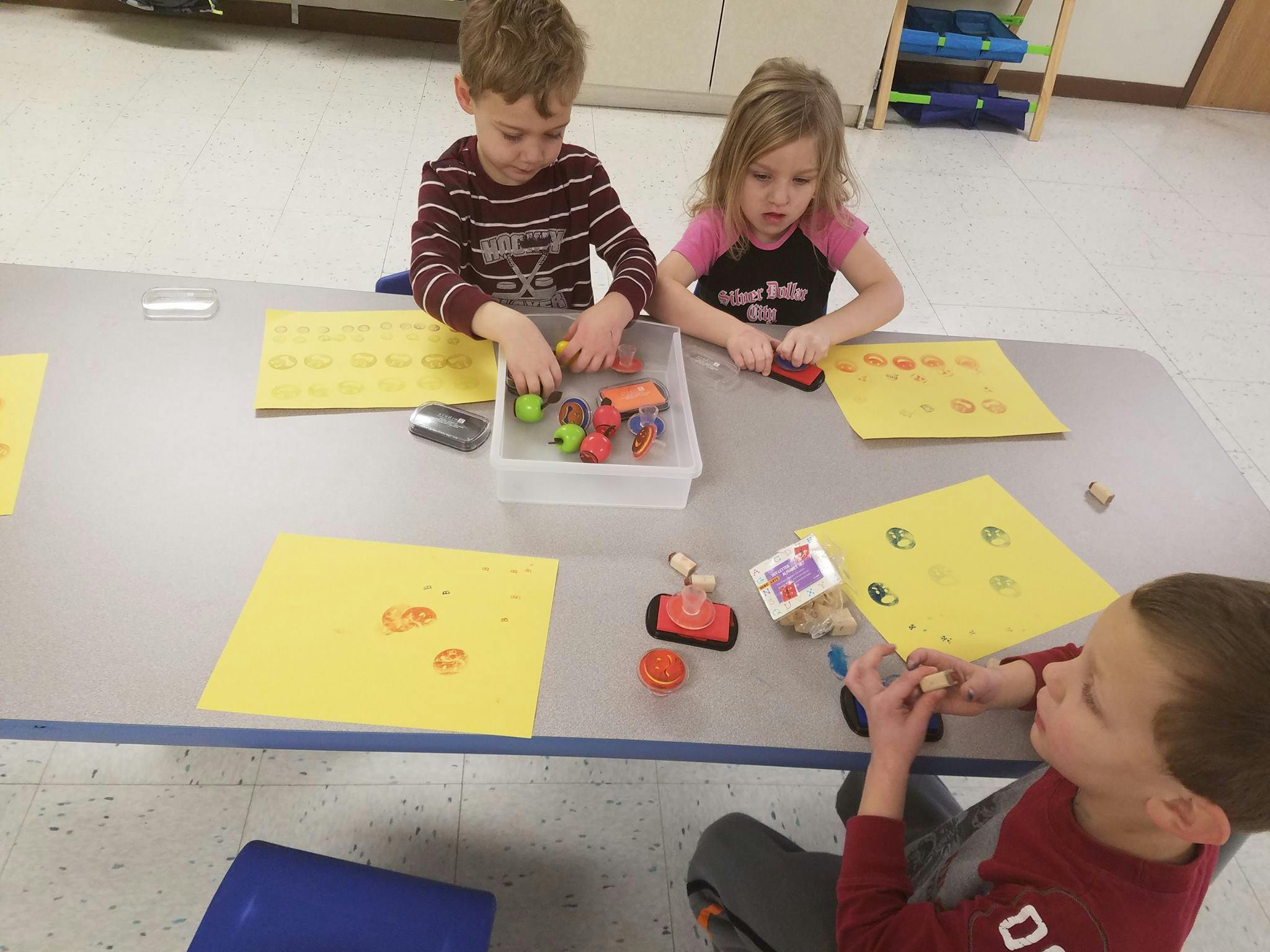 Three children at a table with yellow papers and craft supplies