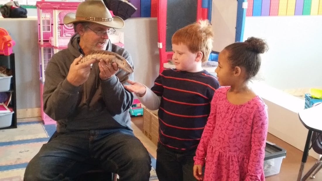 Person in hat holding an animal with two children watching