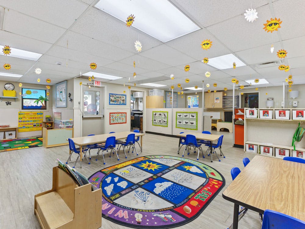 Classroom with small tables and chairs, a circular rug, and sun decorations hanging from the ceiling