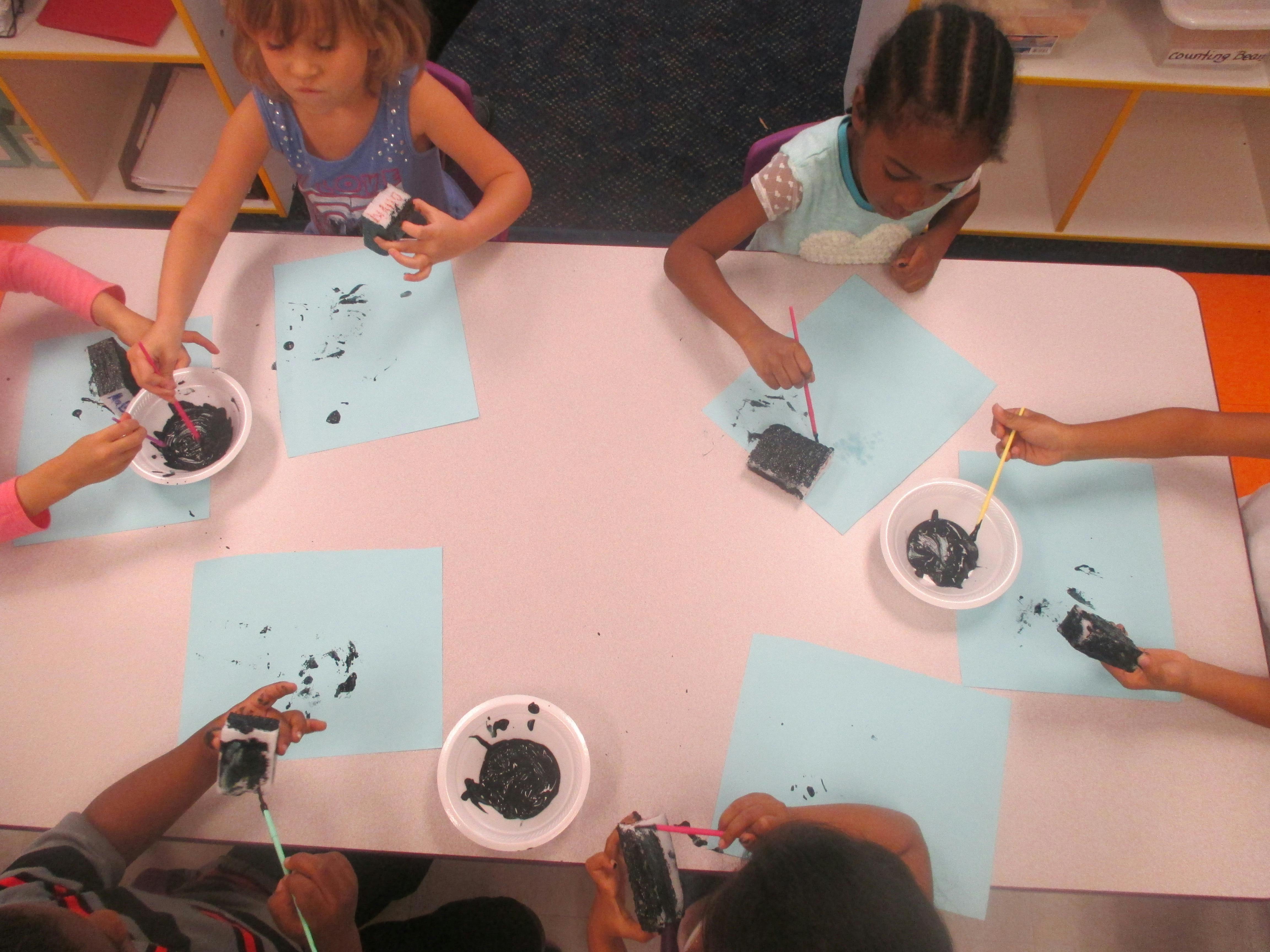 Children painting with sponges and black paint on light blue paper