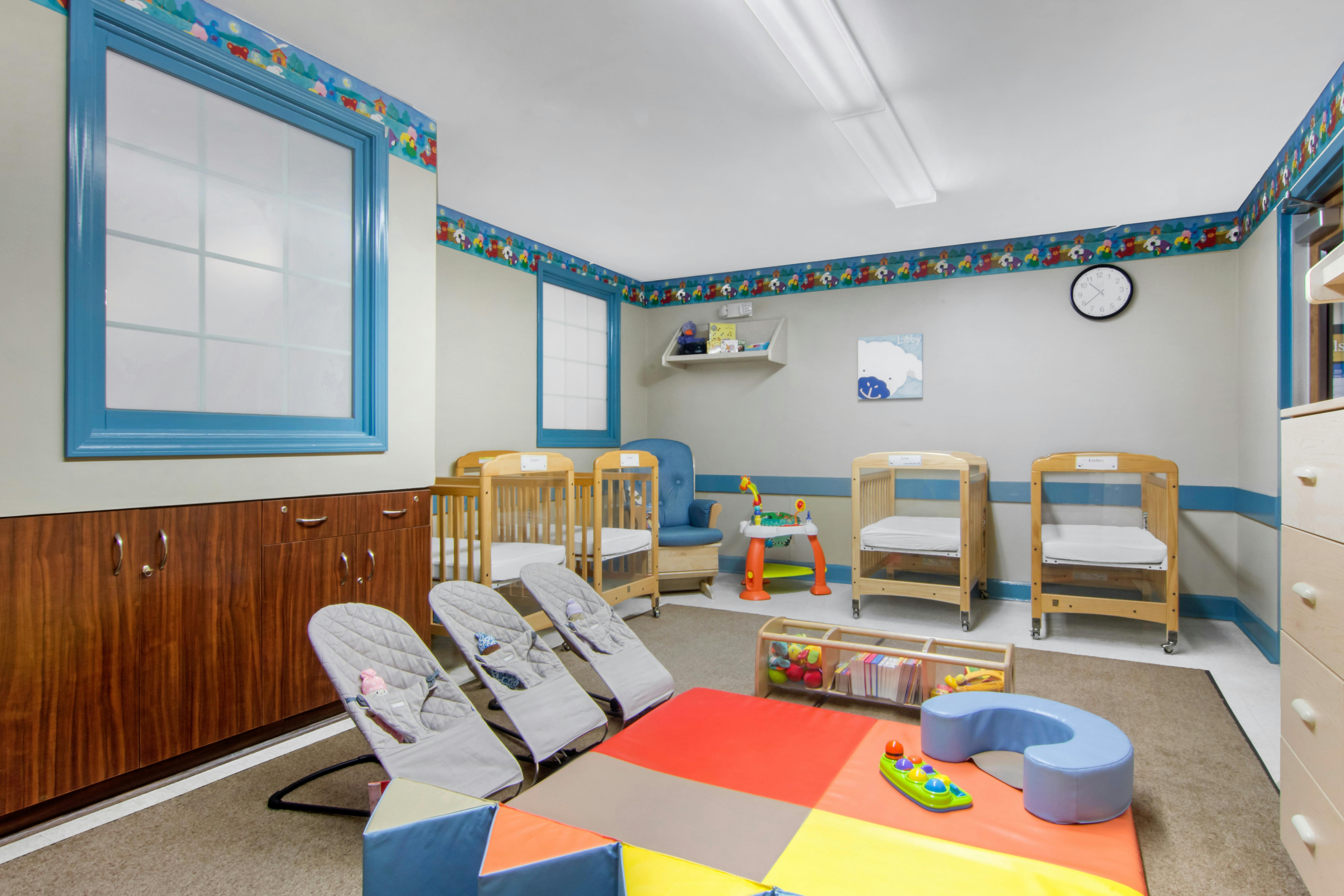 A room with several cribs, baby bouncers, and colorful play mats