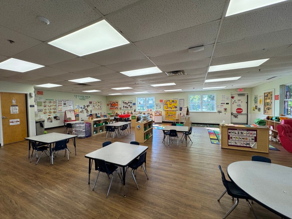 Empty classroom with small tables and chairs, and bright walls decorated with learning materials