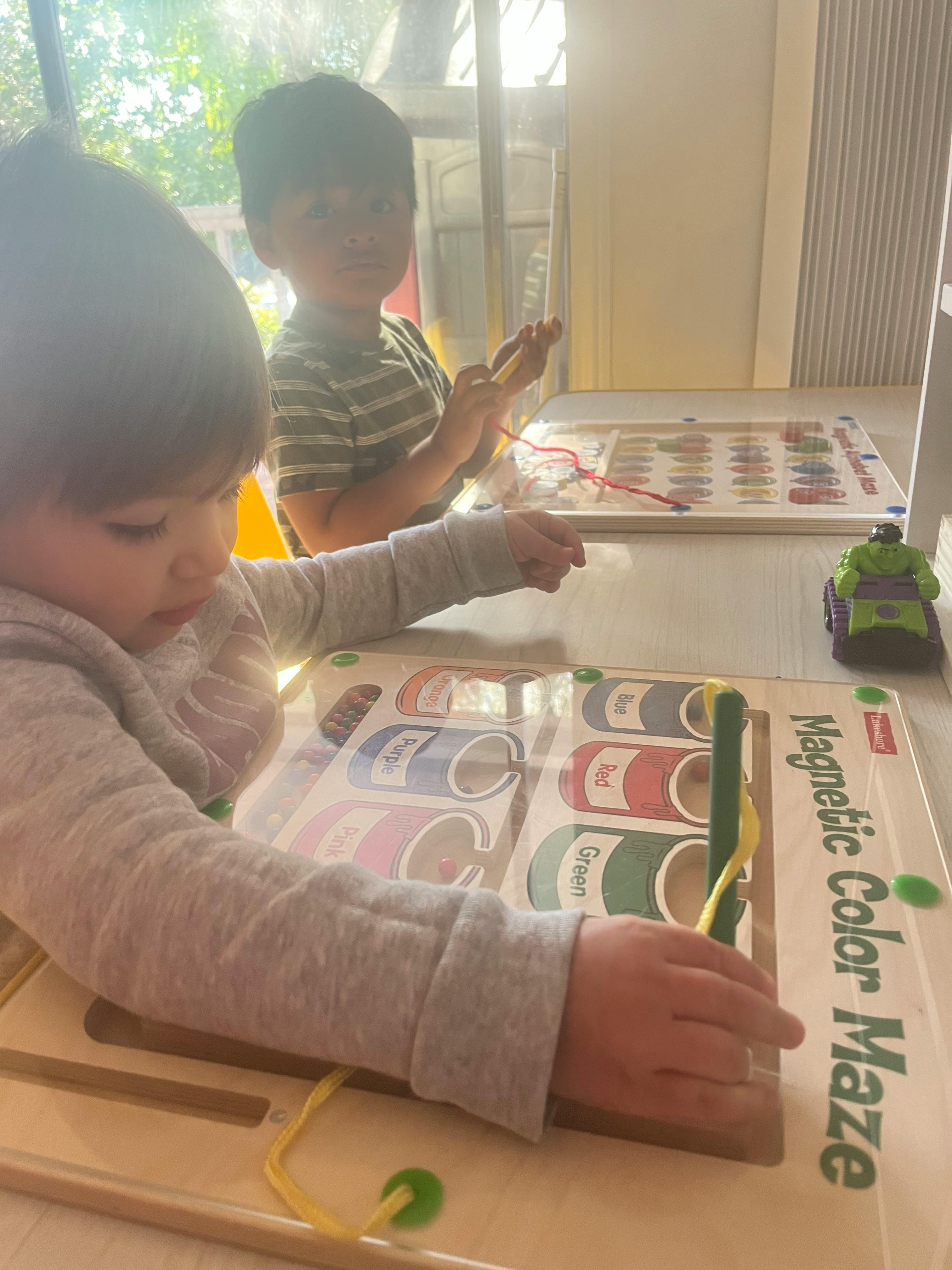 Two children playing with magnetic color maze boards