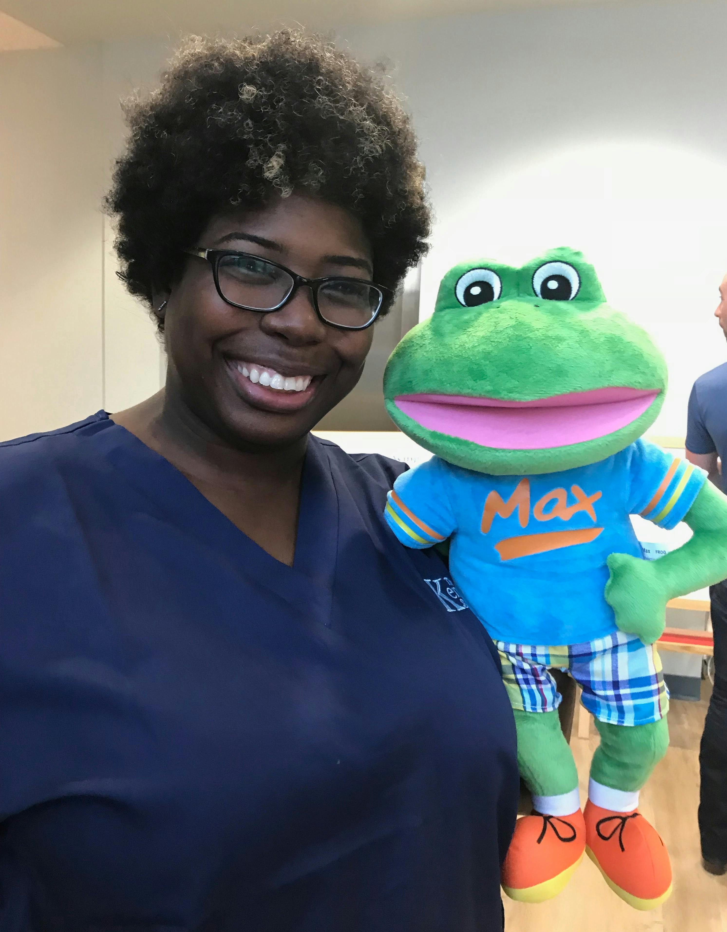 Person in glasses smiling next to a frog puppet wearing a shirt that says Max