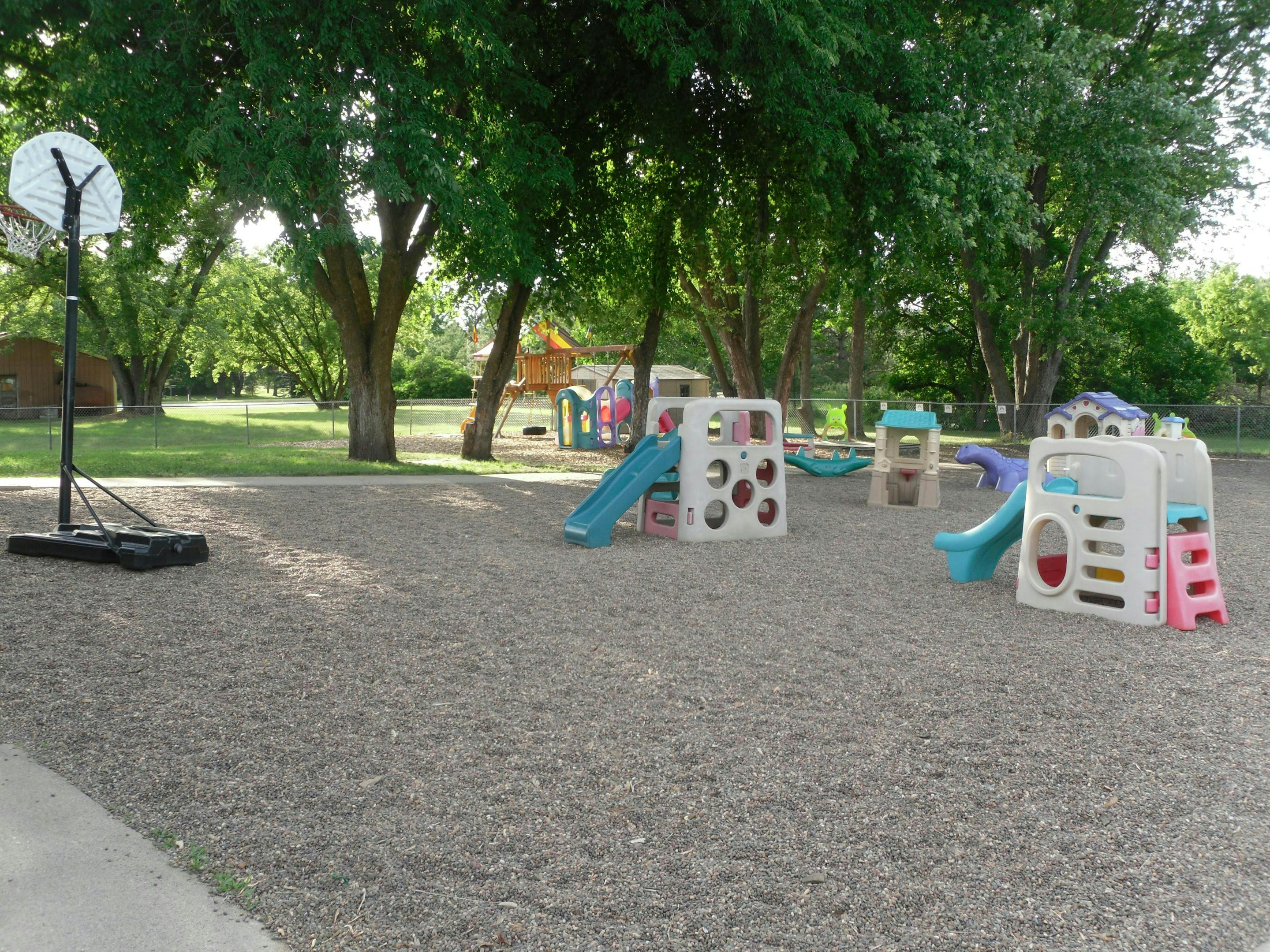 Playground with slides and climbing structures on wood chips, basketball hoop nearby