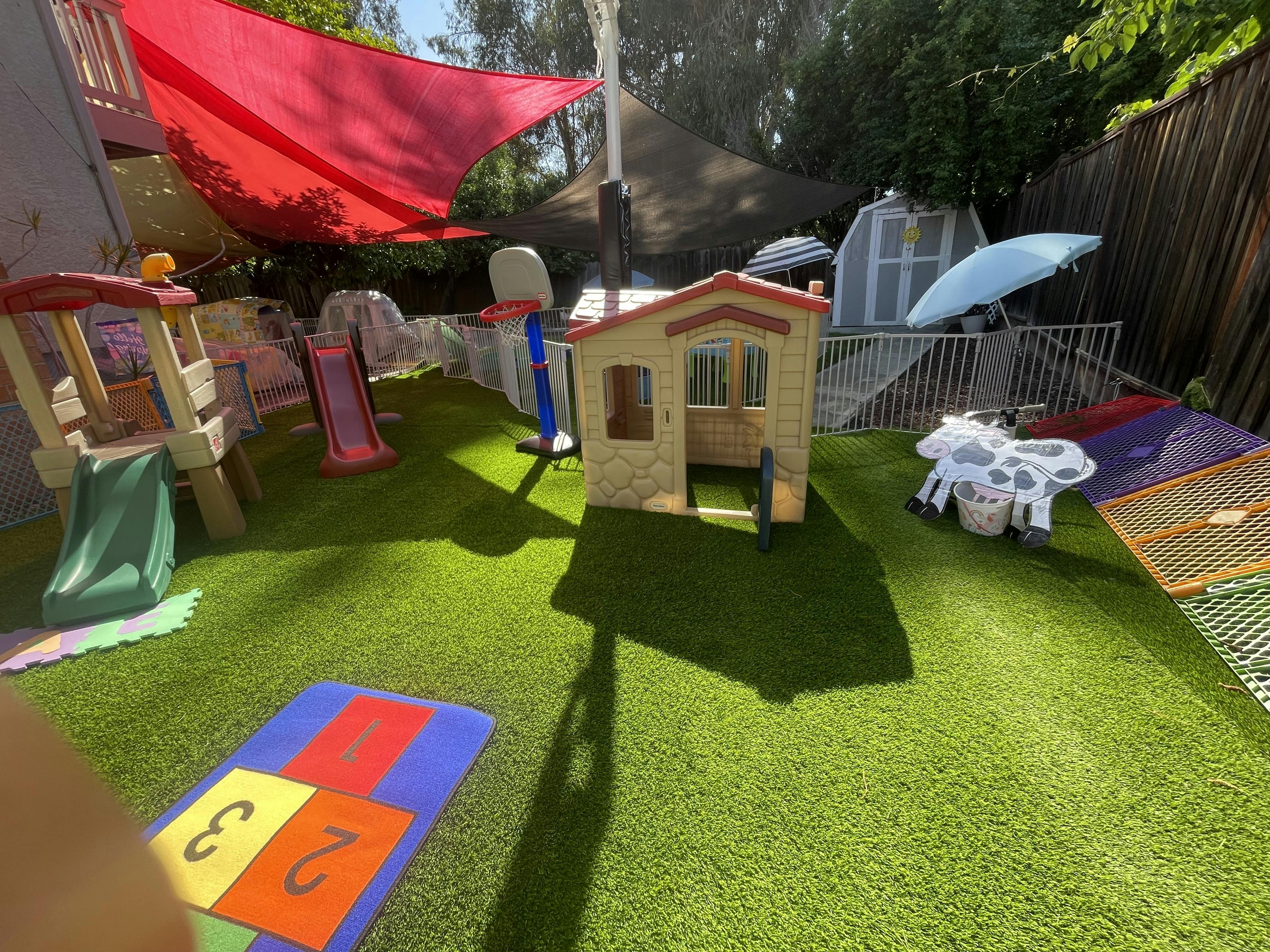 Backyard playground with a playhouse, slides, and shaded areas