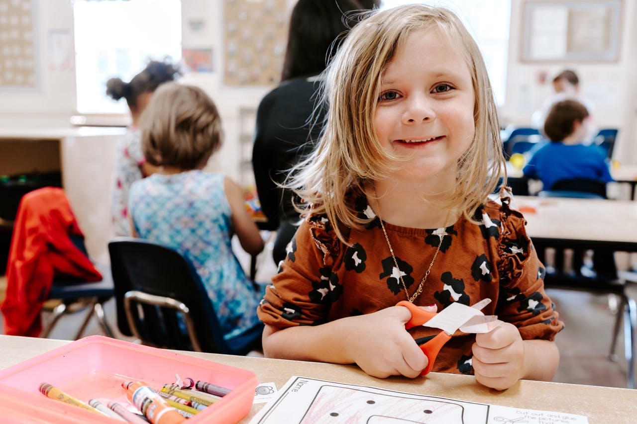 Child cutting paper with scissors in a classroom