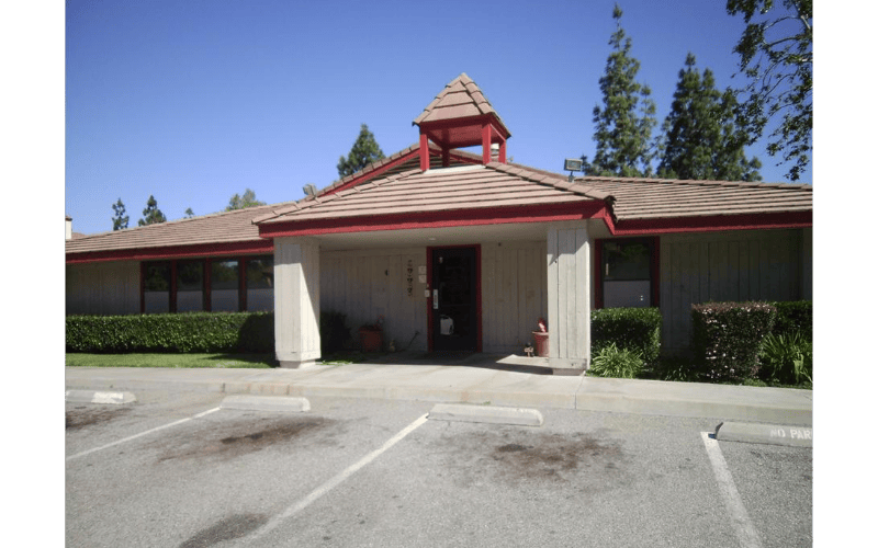 Building with a red-trimmed roof and a small steeple over the entrance, and a parking lot