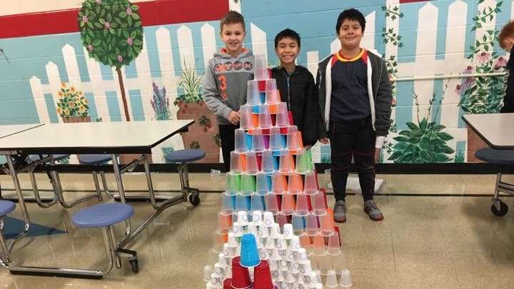 Three children standing next to a large pyramid made of colorful plastic cups