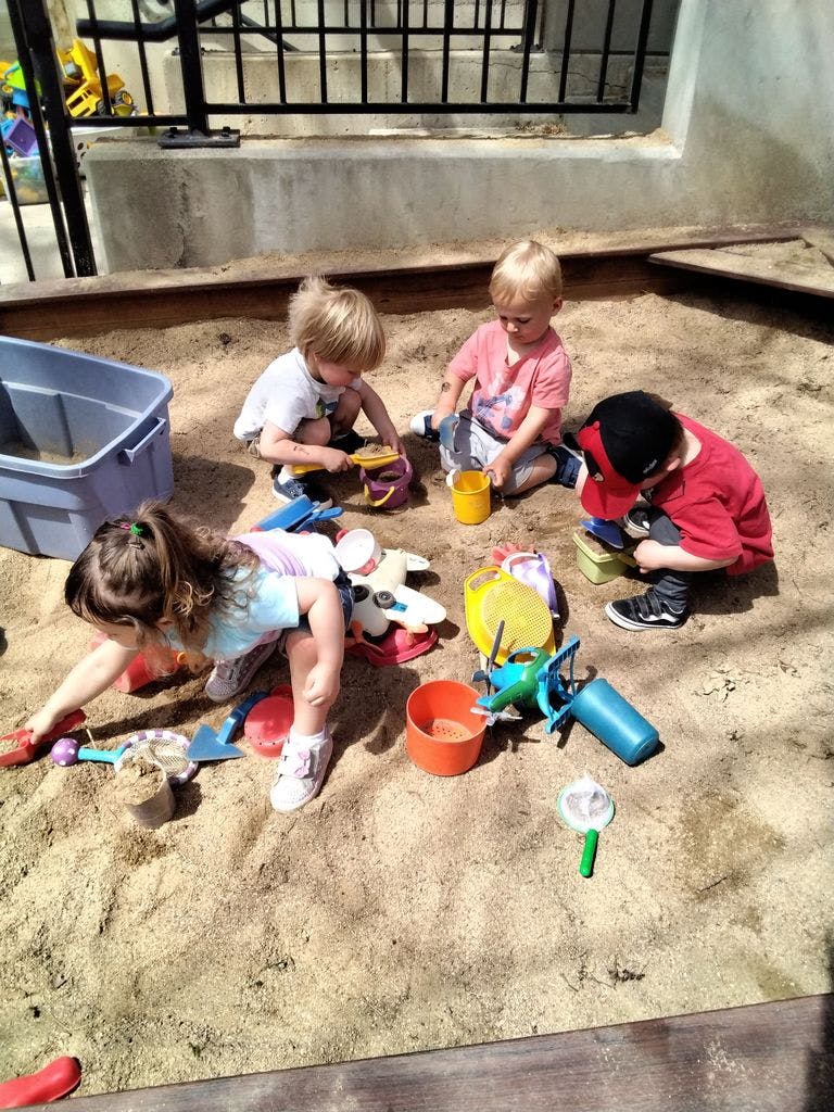 Four children playing in a sandbox with toys