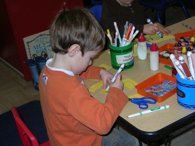 Child drawing with a marker at a table with art supplies