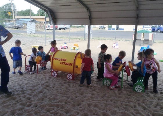 Children playing with toys in a sand-covered area under a canopy