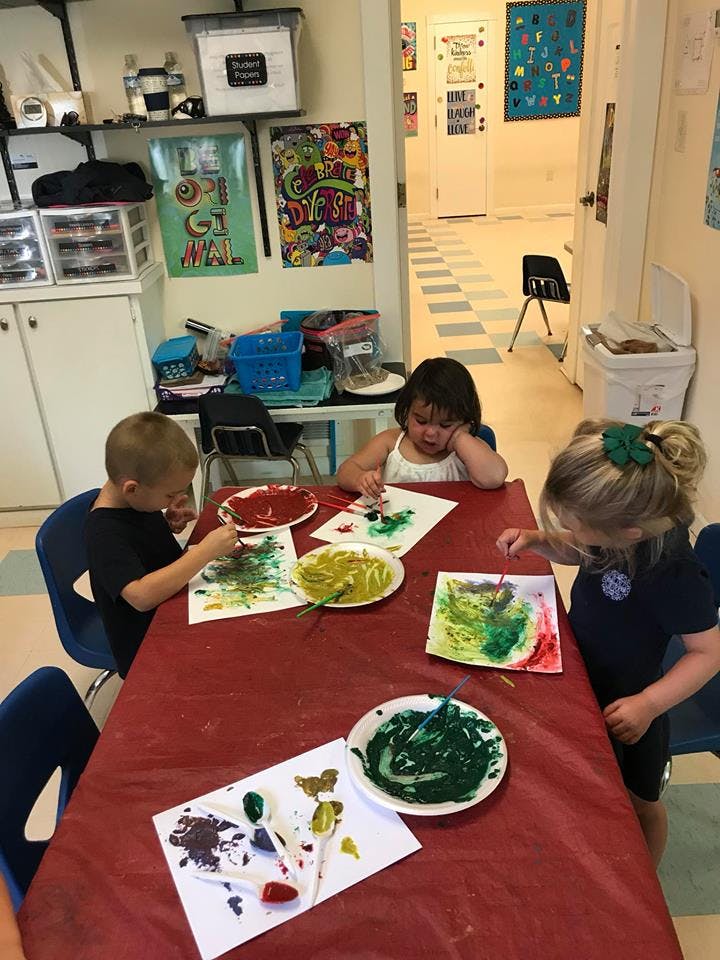 Three children painting at a table in a classroom
