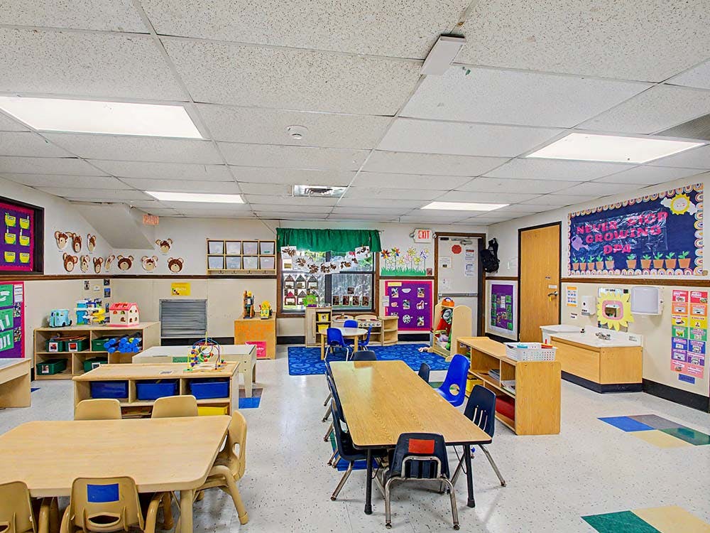 Empty colorful preschool classroom with small tables, chairs, and learning decorations