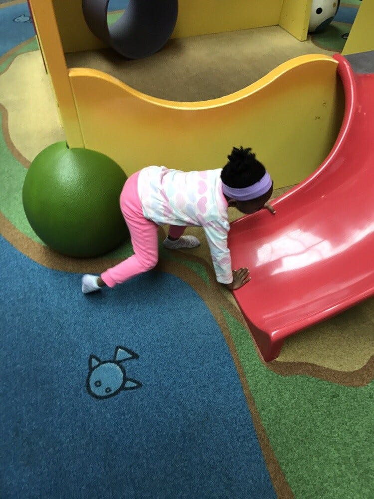 Child crawling on a colorful playground surface next to a red slide