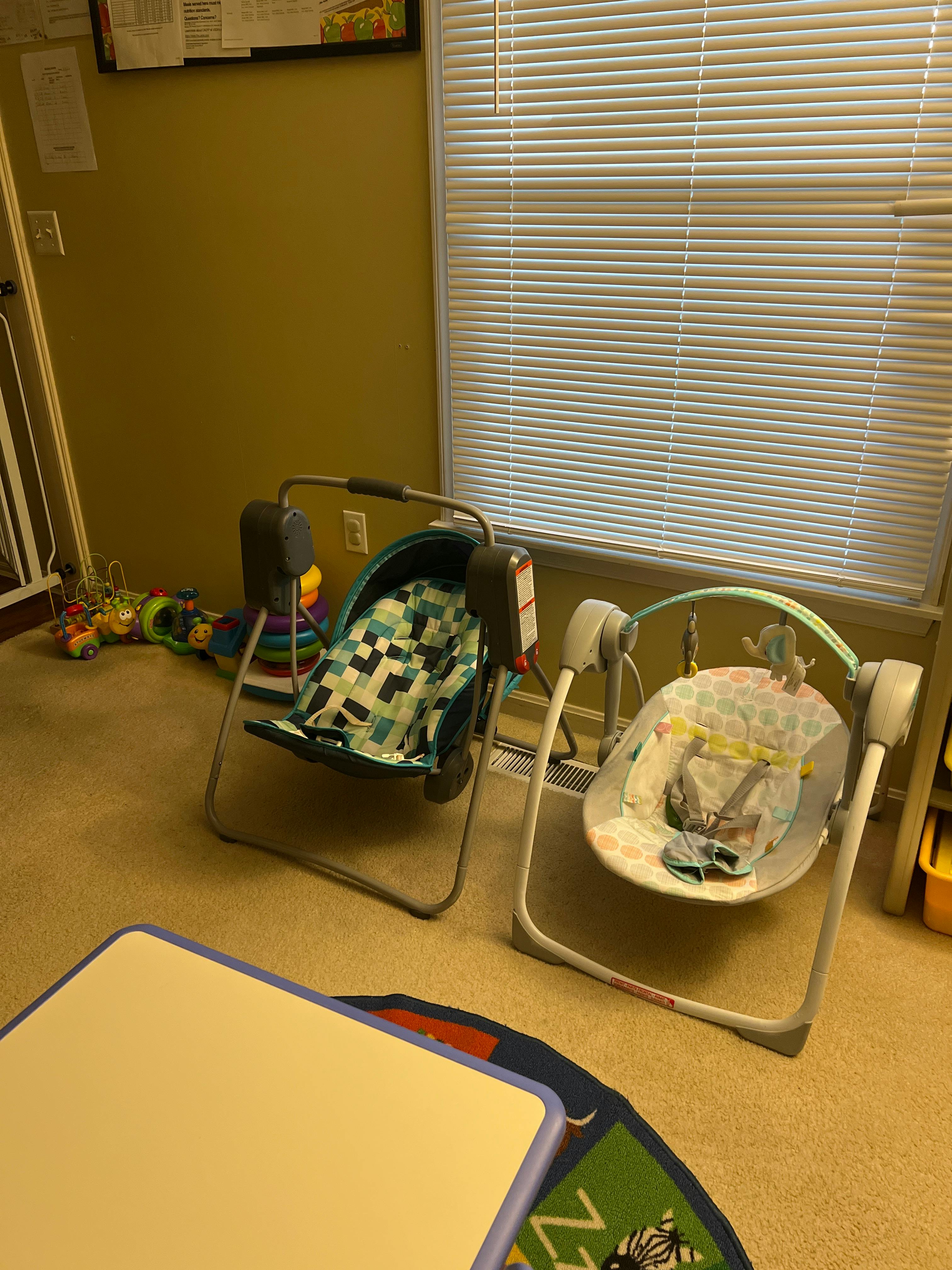 Two empty baby swings and a colorful rug on a carpeted floor