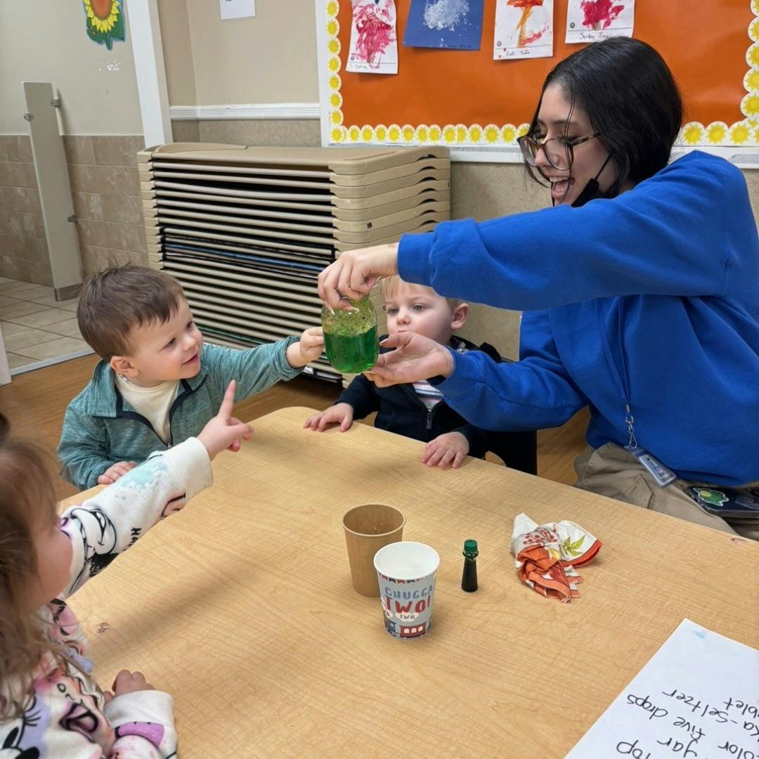 Person pouring liquid into a child's cup at a table with other children