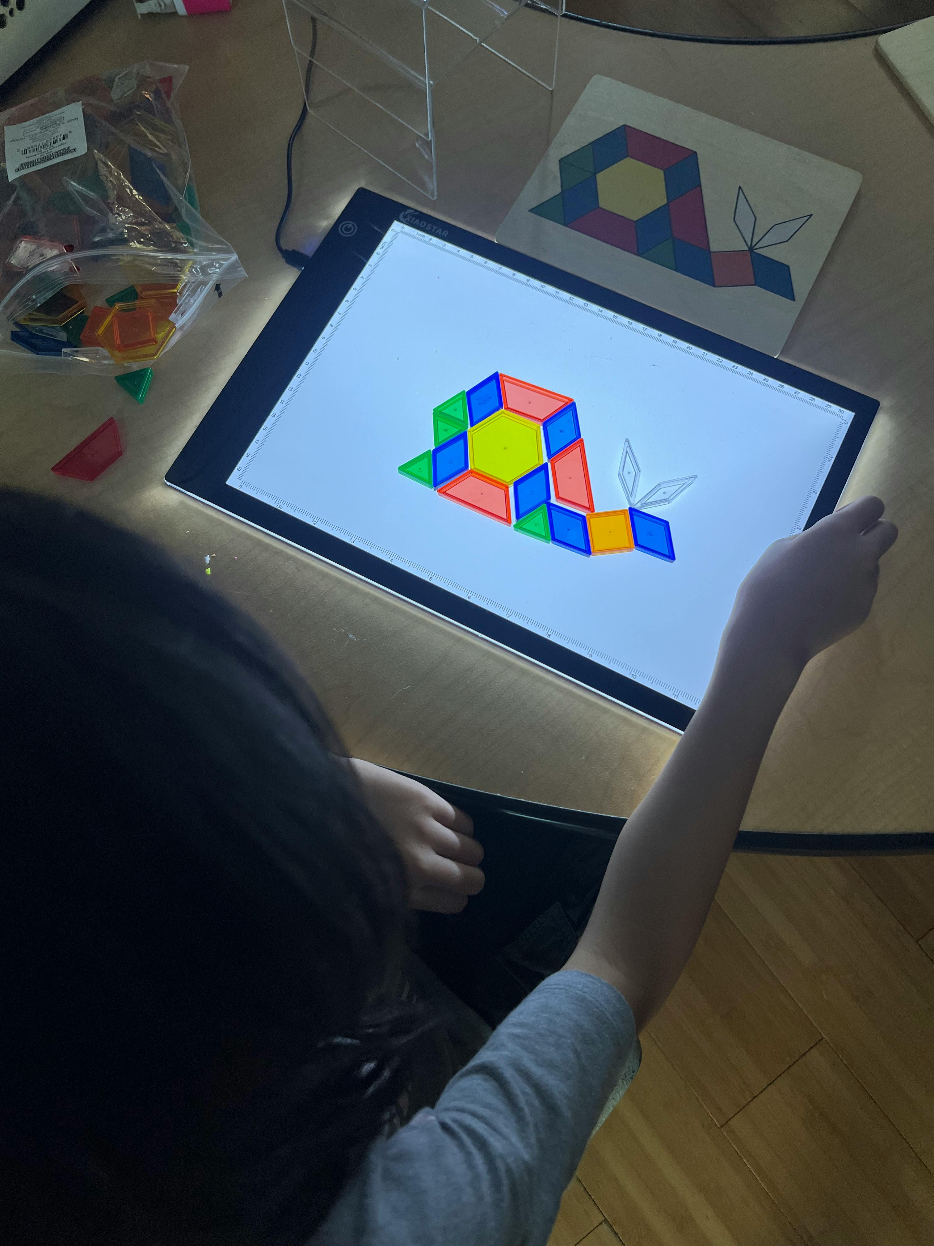 Child creating a snail design with colorful geometric shapes on a light board