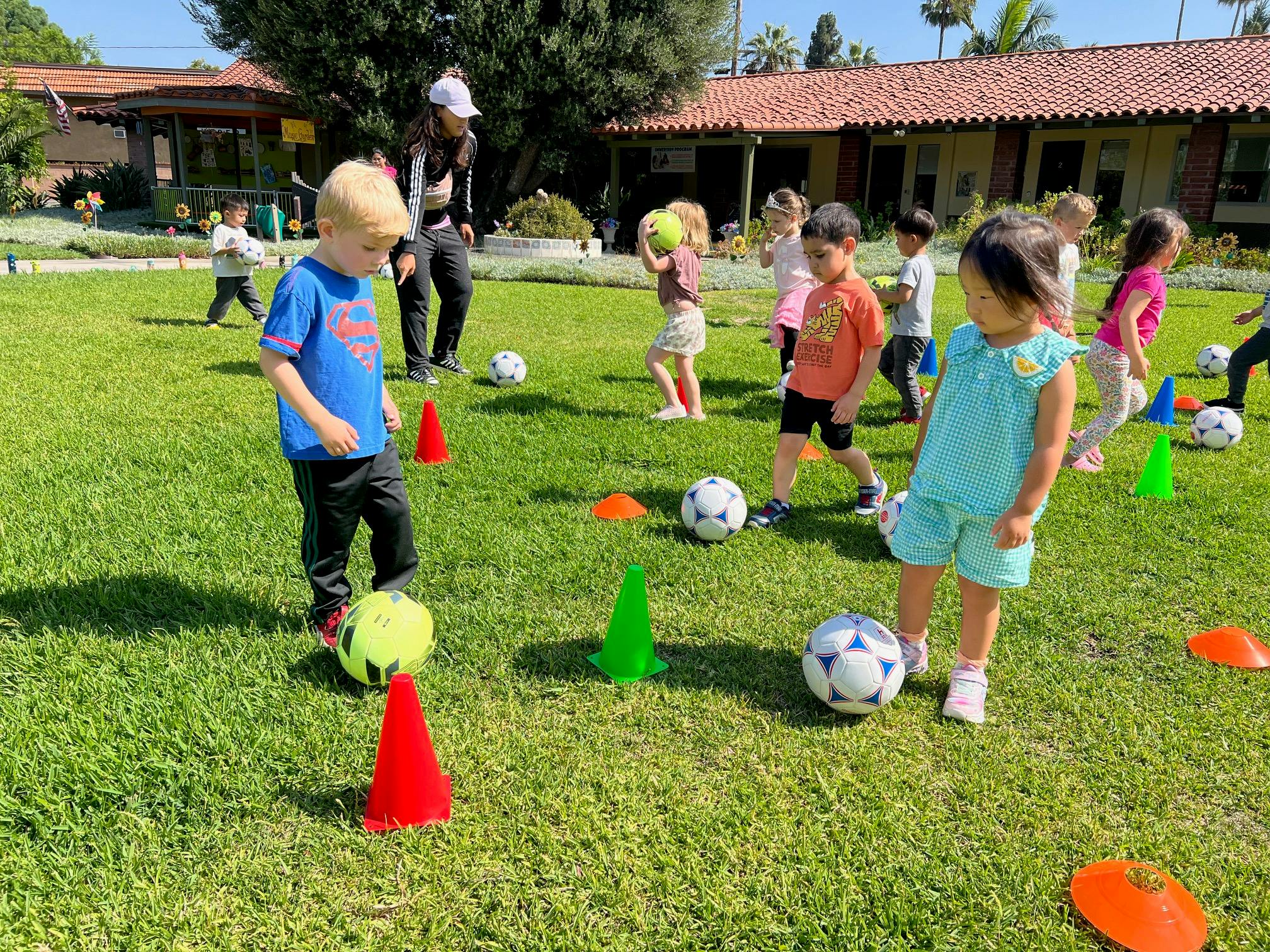 Children playing soccer with cones and balls on a grassy field