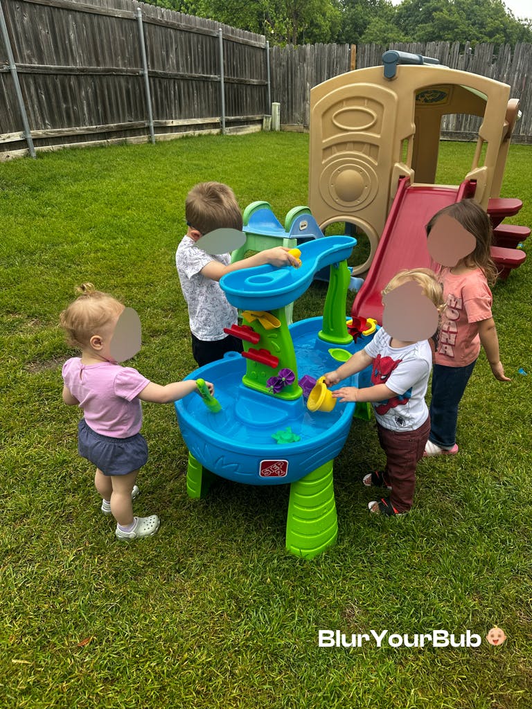 Four children playing around a water table in a grassy yard