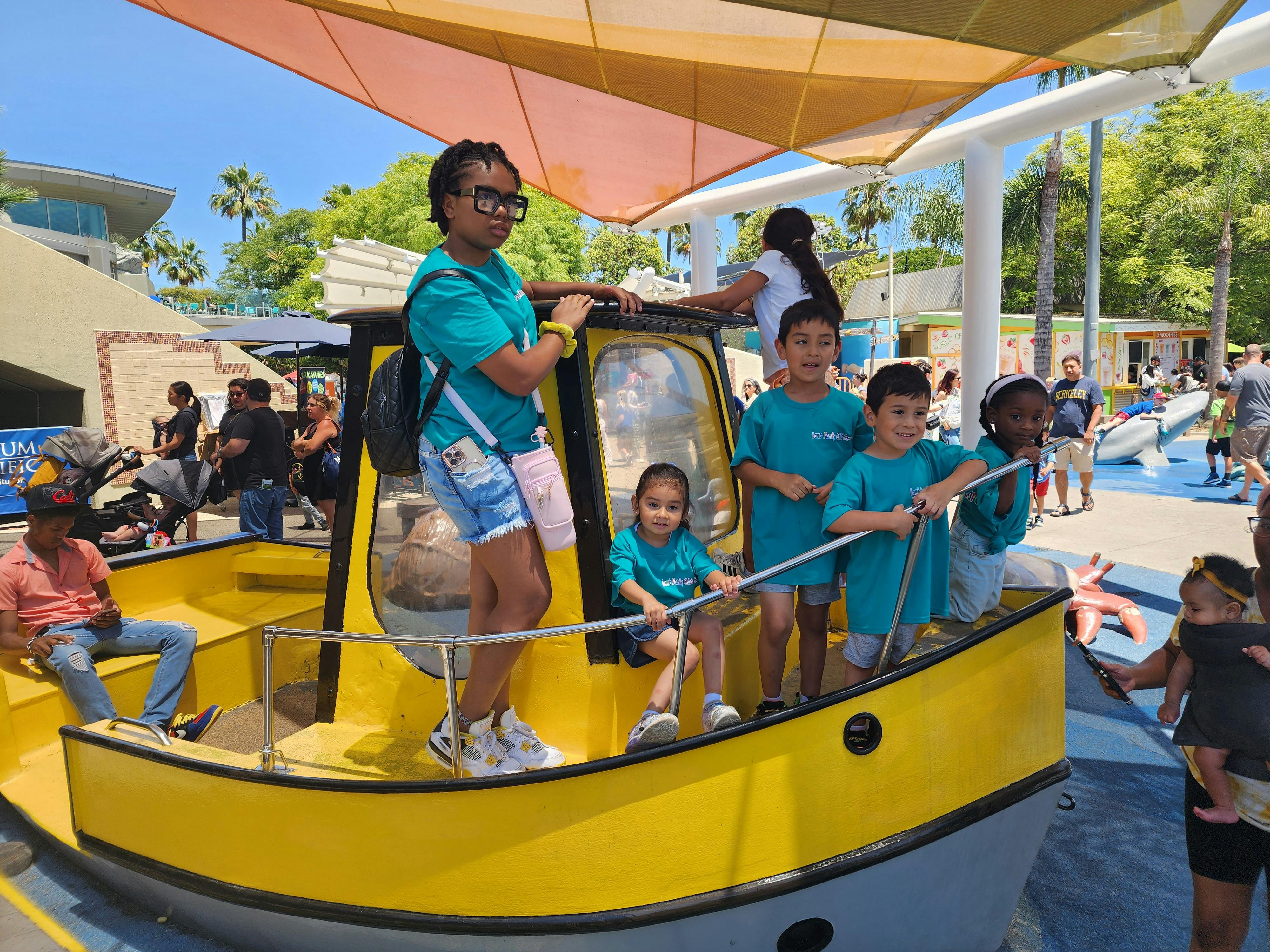 People and children standing on and around a yellow boat on a sunny day