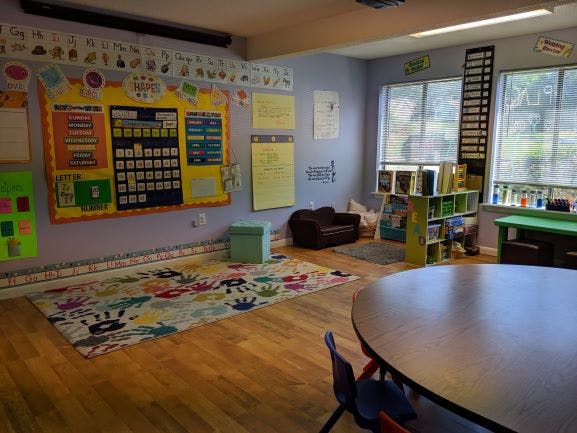 Classroom with a colorful rug, bulletin board, and small furniture