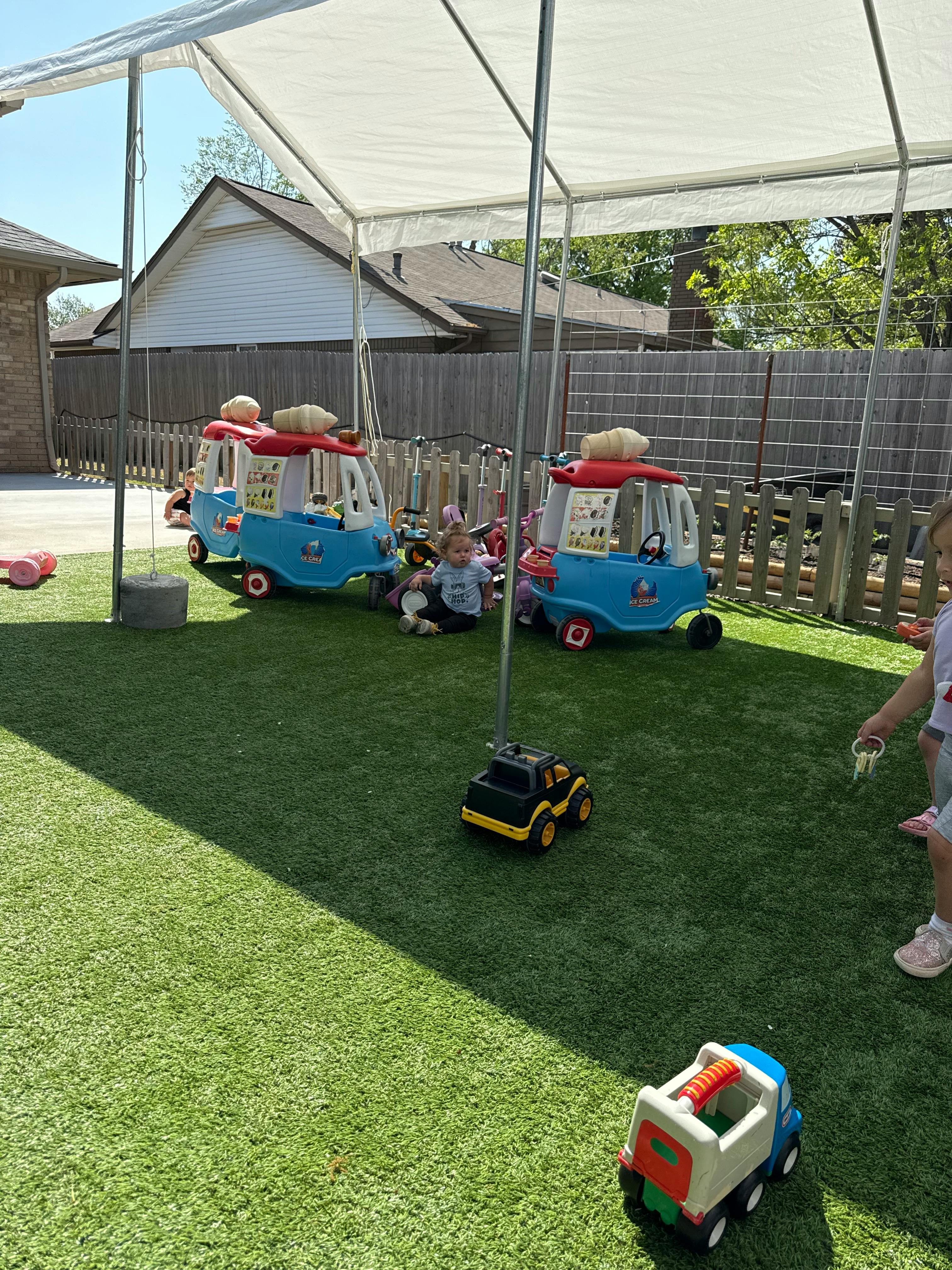 Child playing with toy cars on artificial grass under a canopy