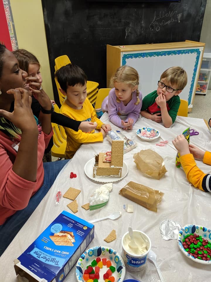 Adult and children making gingerbread houses at a table