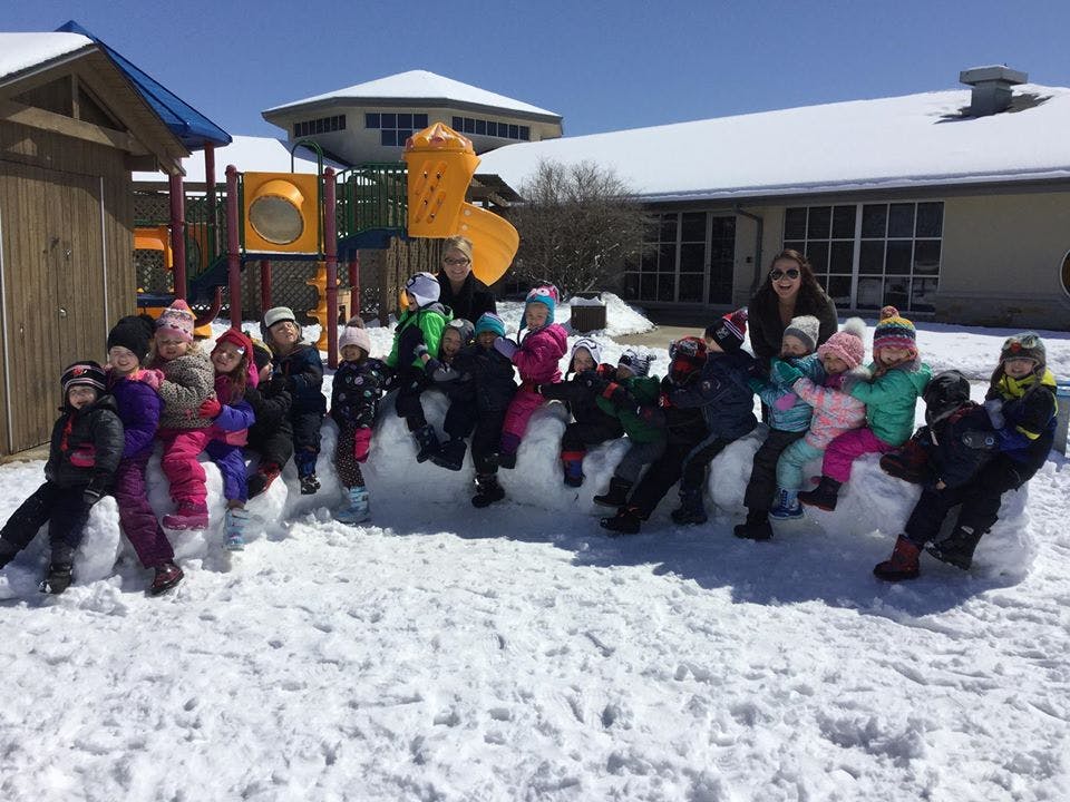 Children and adults sitting on snow sculptures in a snowy playground