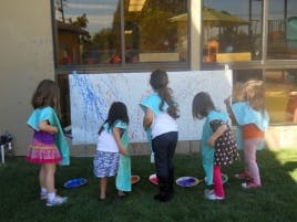 Children painting on a large white canvas outdoors