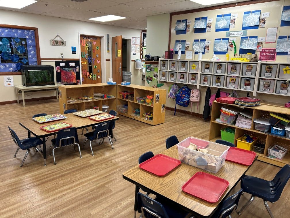 Classroom with small tables and chairs, shelves with toys, and artwork on walls