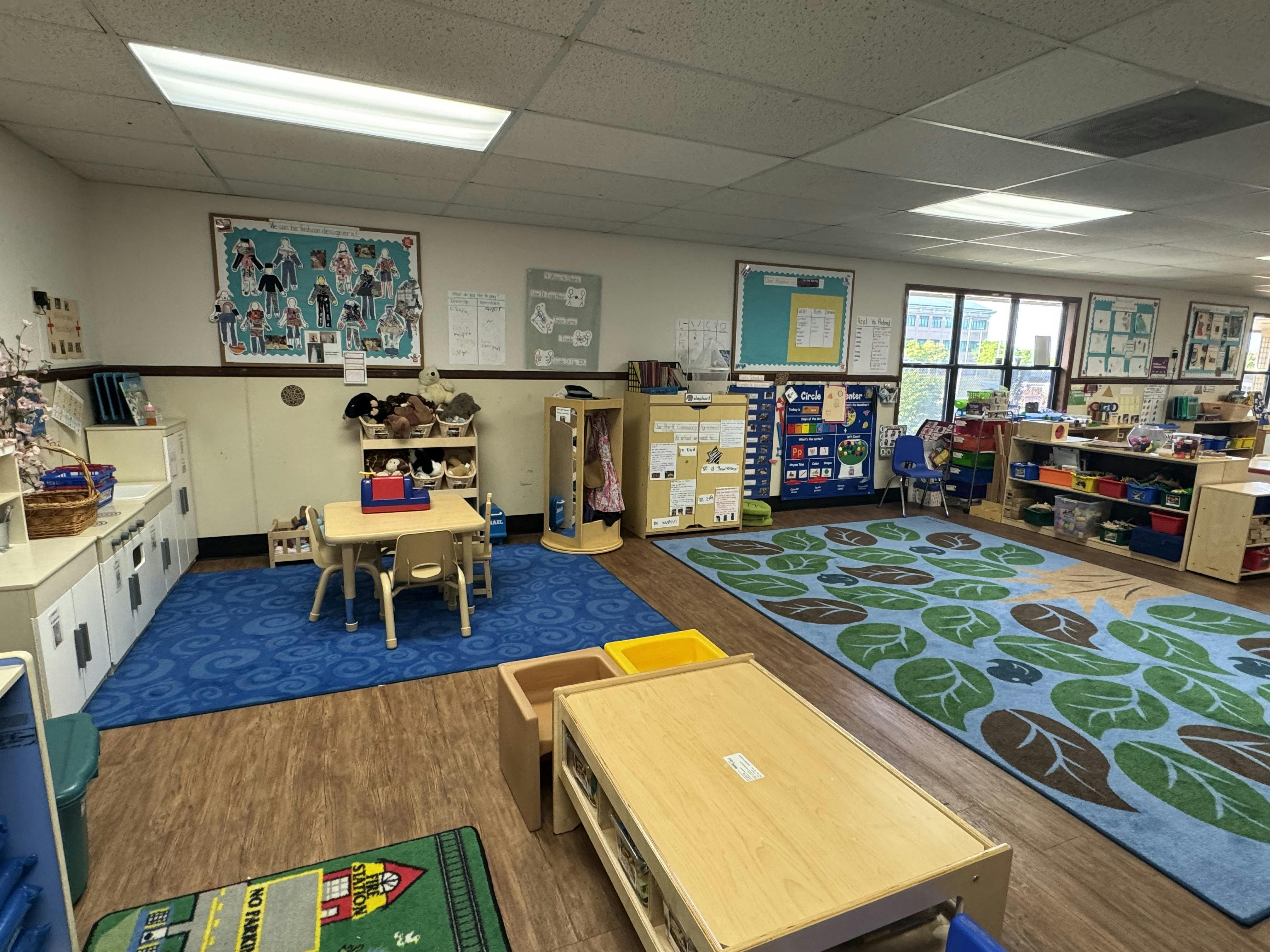 Empty classroom with small tables and chairs, play kitchen, colorful rugs