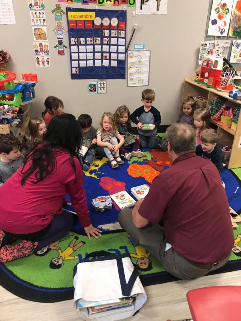 Adults and children sitting on a rug in a classroom