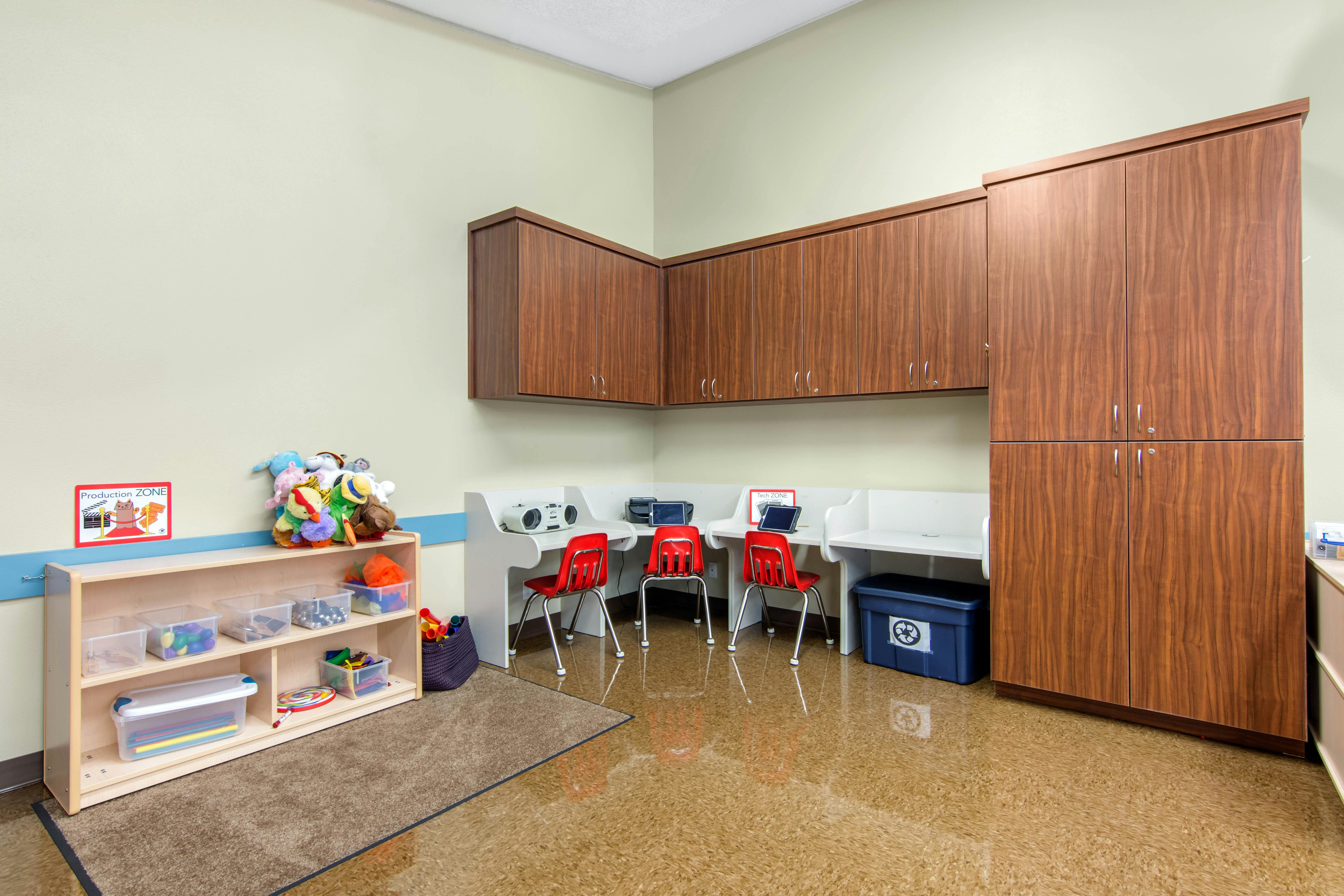Classroom corner with wooden cabinets, small red chairs, and a toy shelf