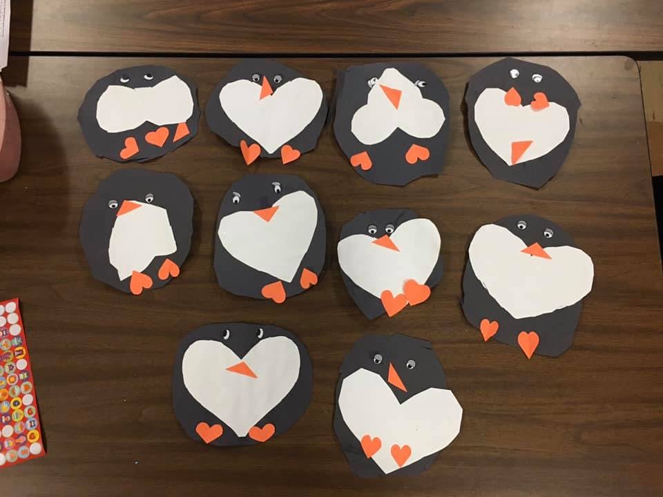 Multiple paper cutouts of penguins with heart-shaped white bellies