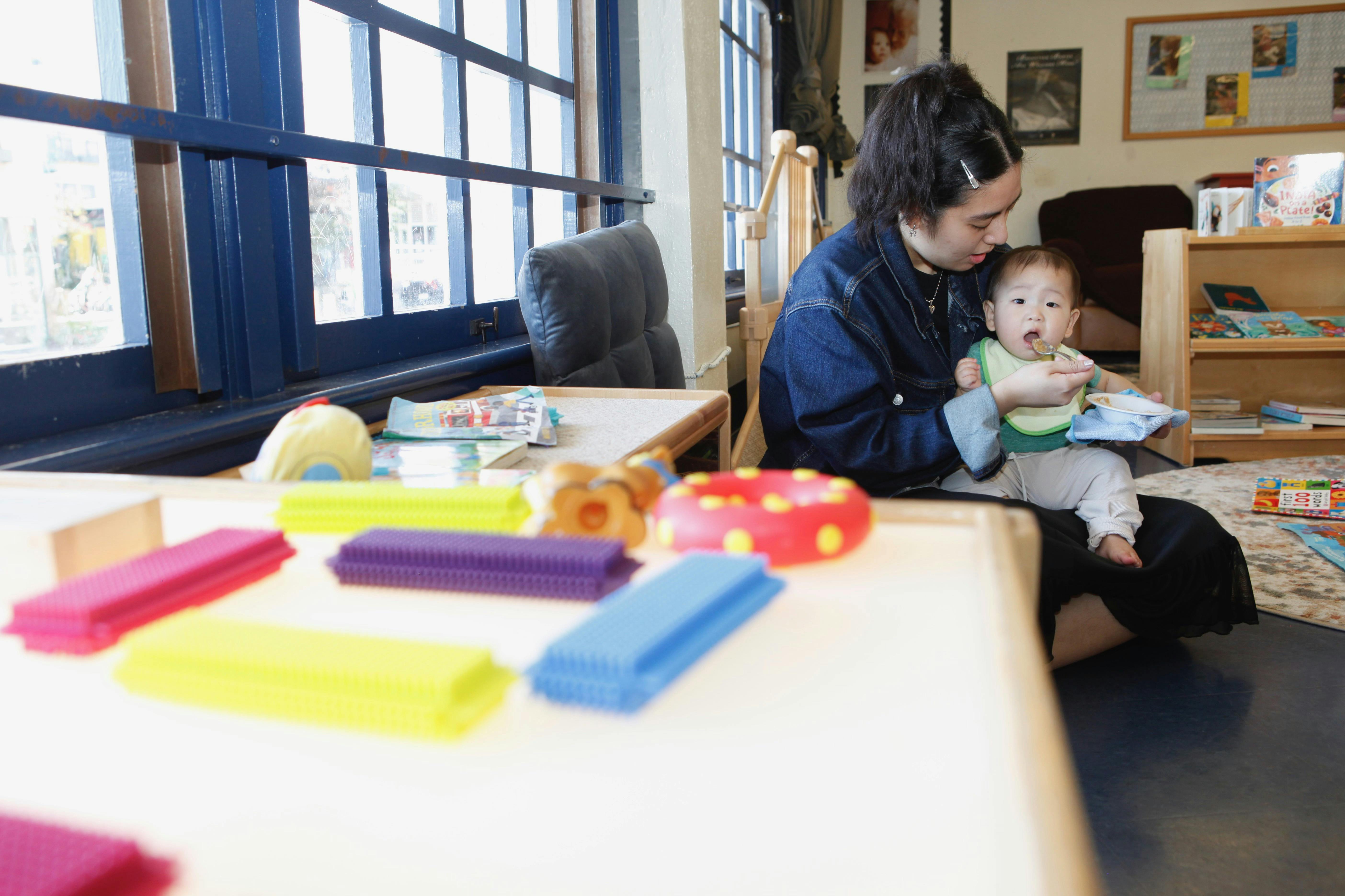 Person holding a baby in a room with toys on a table