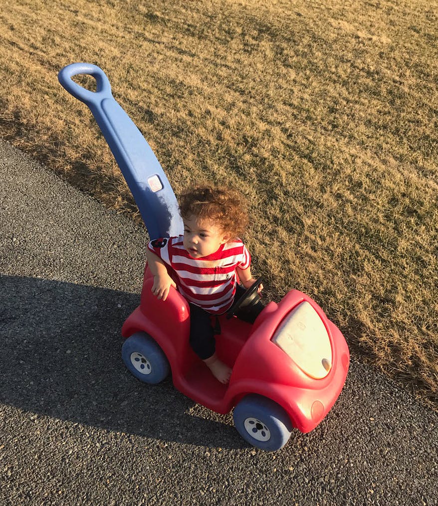 Child in a red toy car with a blue handle