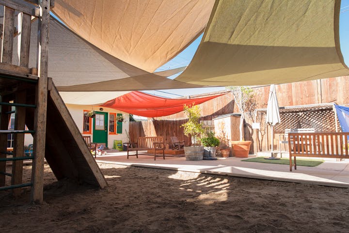 Outdoor play area with shade sails, a wooden play structure, and patio furniture